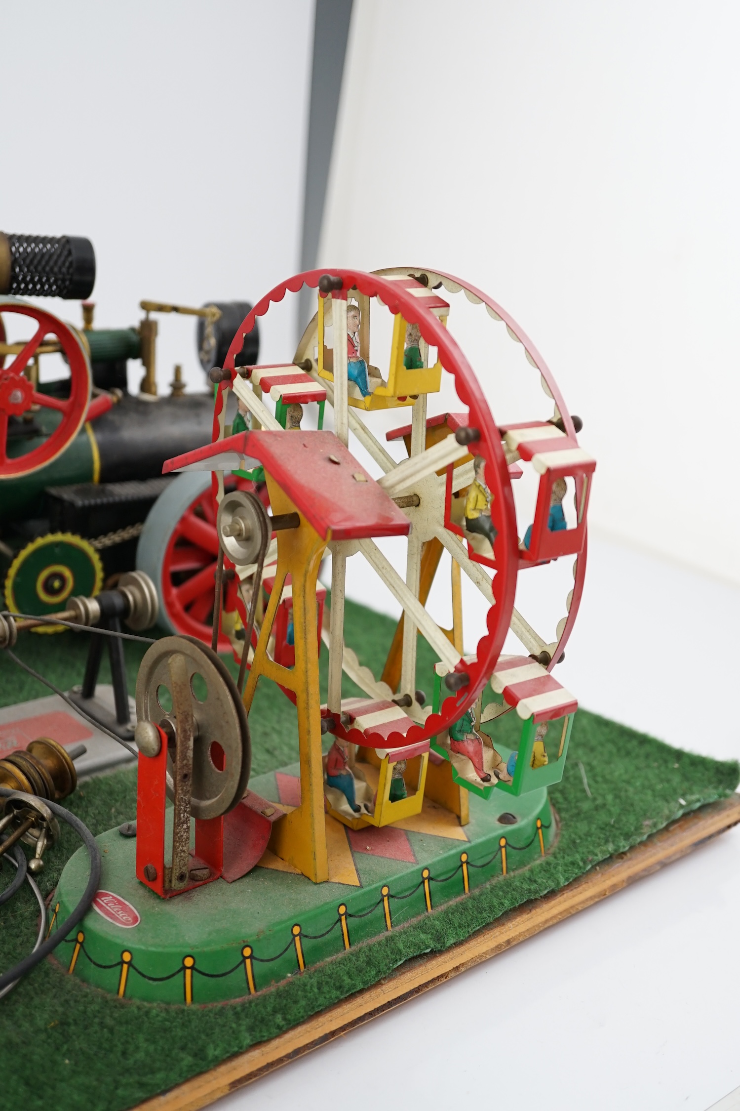 A Wilesco live steam fairground diorama, comprising a D430 pellet fired traction engine, powering a pulley and gear assembly, in turn running three tinplate fairground rides, mounted on a plywood sheet topped with grass